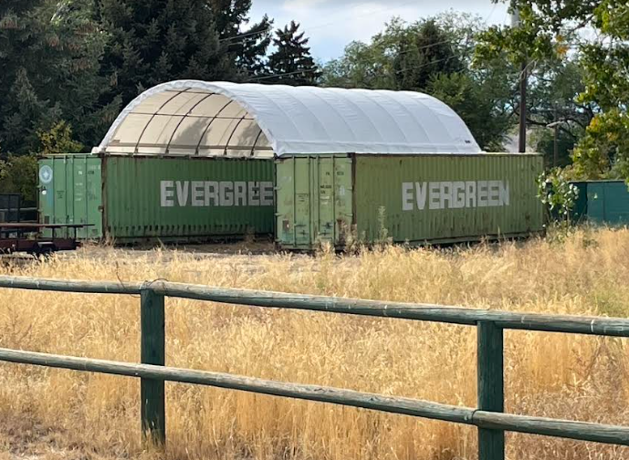 White PVC container shelter arched over two green shipping containers, galvanized frame open at the end