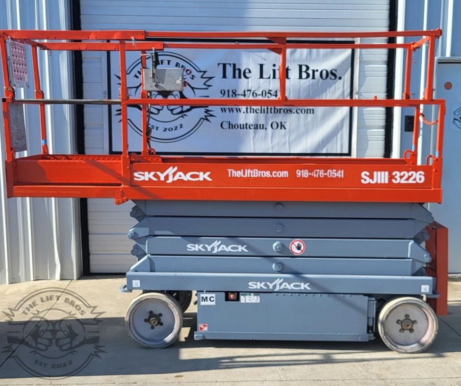Orange SkyJack SJIII 3226 scissor lift, platform lowered with guardrails and roll-out deck extension, gray scissor stack