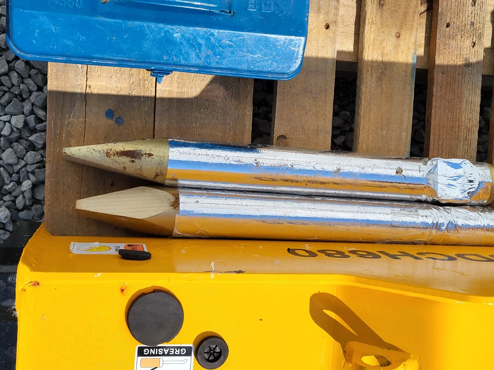 Two foil-wrapped chisels with pointed and wedge tips resting on the SDCH680's yellow body beside the tool box