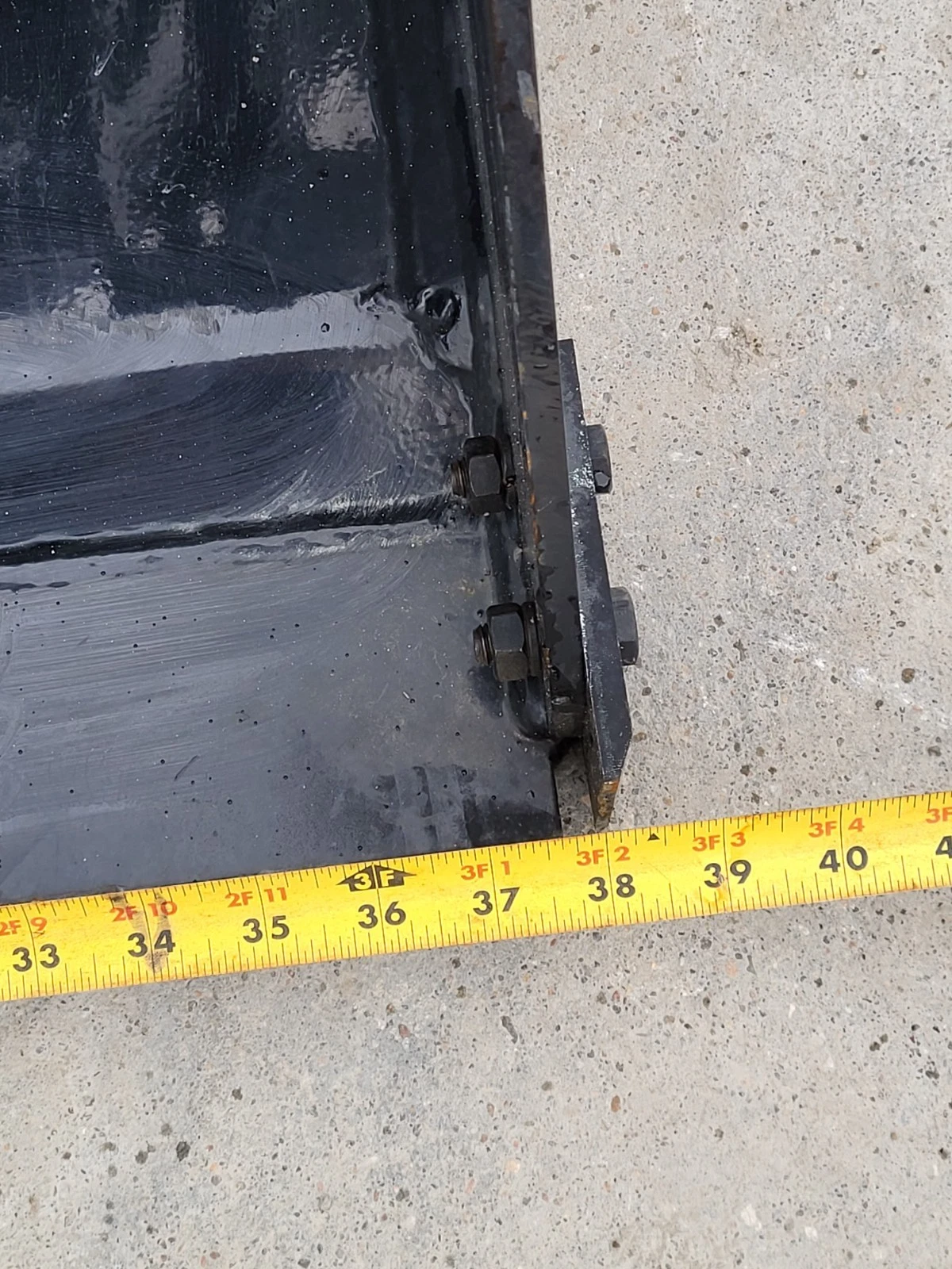 Tape measure at the 4-in-1 bucket's bottom corner reading 38 inches across the bucket width