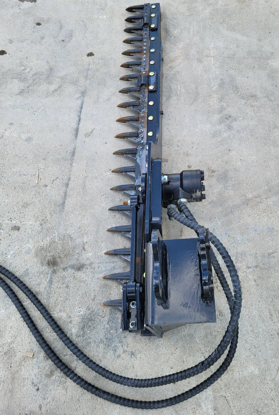 Sickle mower bar stood on end, pointed cutter guards down its length, mount plate and coiled hoses