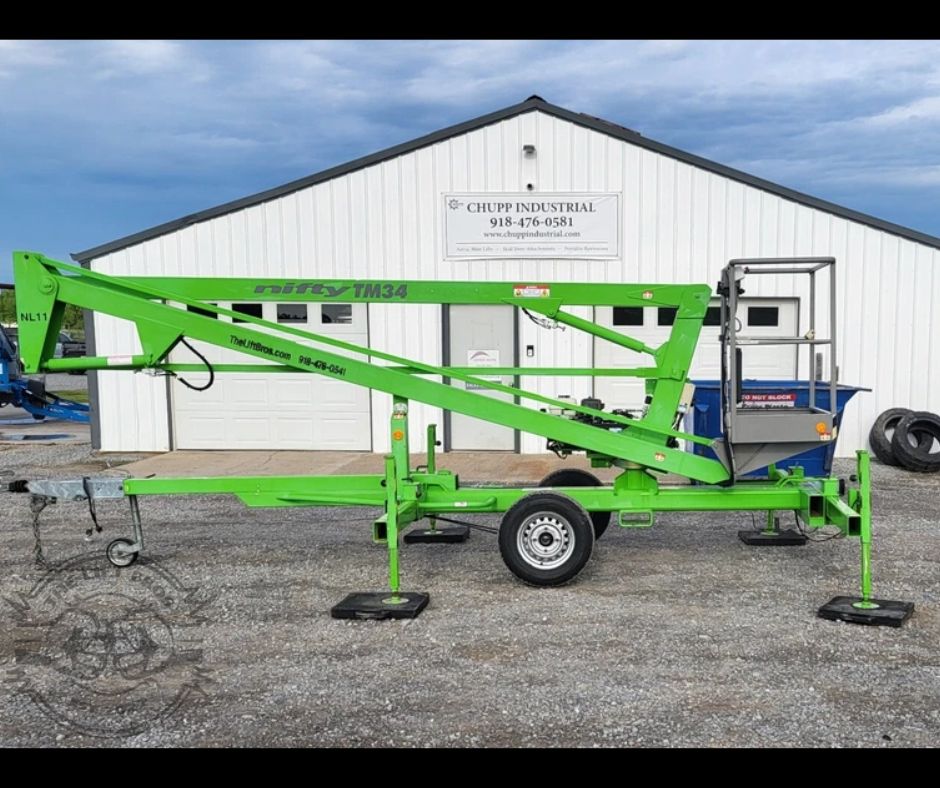 Green Nifty TM34 towable boom lift folded on its trailer with outriggers down and tow coupler