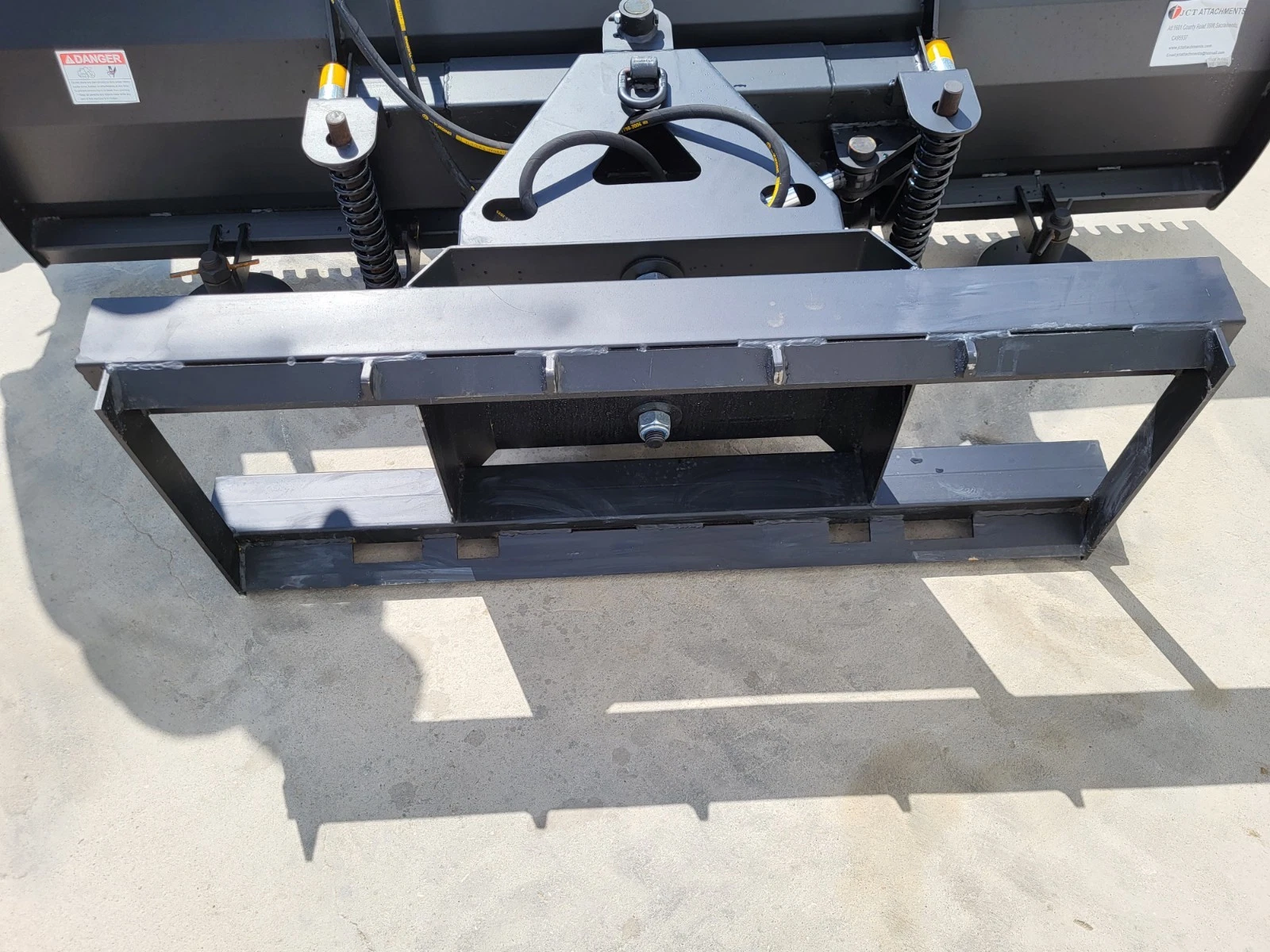 Back of the push blade: white quick-attach plate, dual hydraulic cylinders, coil springs and hand crank