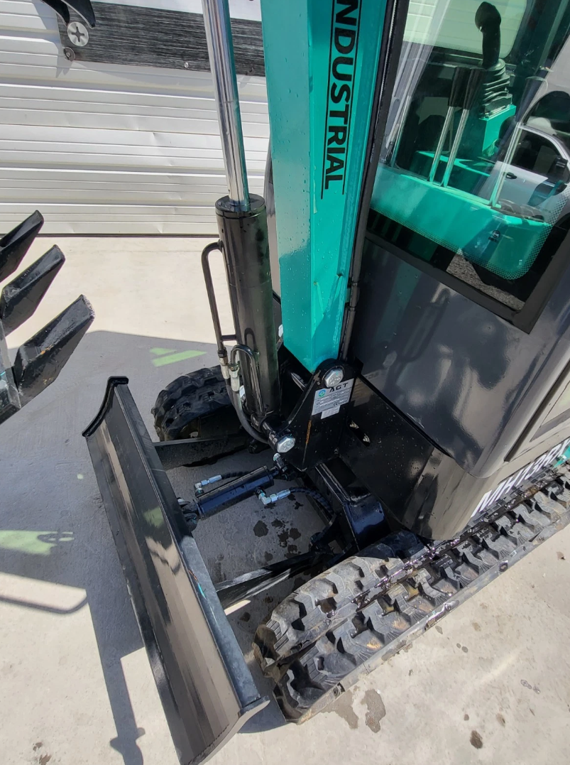 Teal MH13RX mini excavator: boom base and lift cylinder above the dozer blade, rubber tracks and glass cab