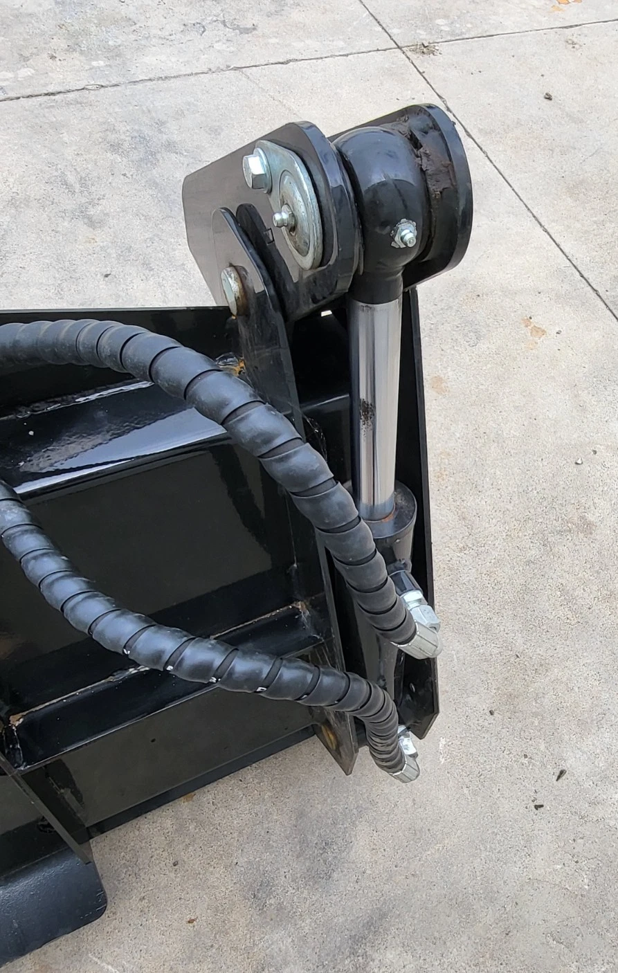 Clam cylinder rod and pivot pin at the corner of the 4-in-1 bucket, hoses running across the shell