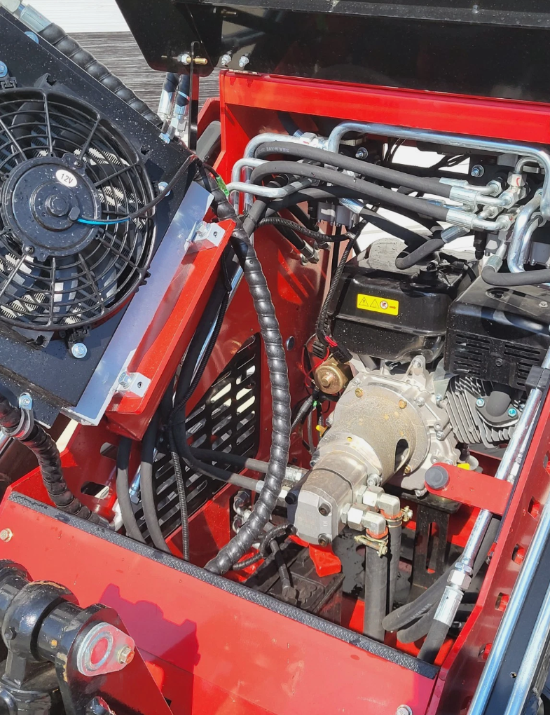 Engine bay of the red mini skid steer: horizontal engine, hydraulic pump and lines, 12V cooling fan