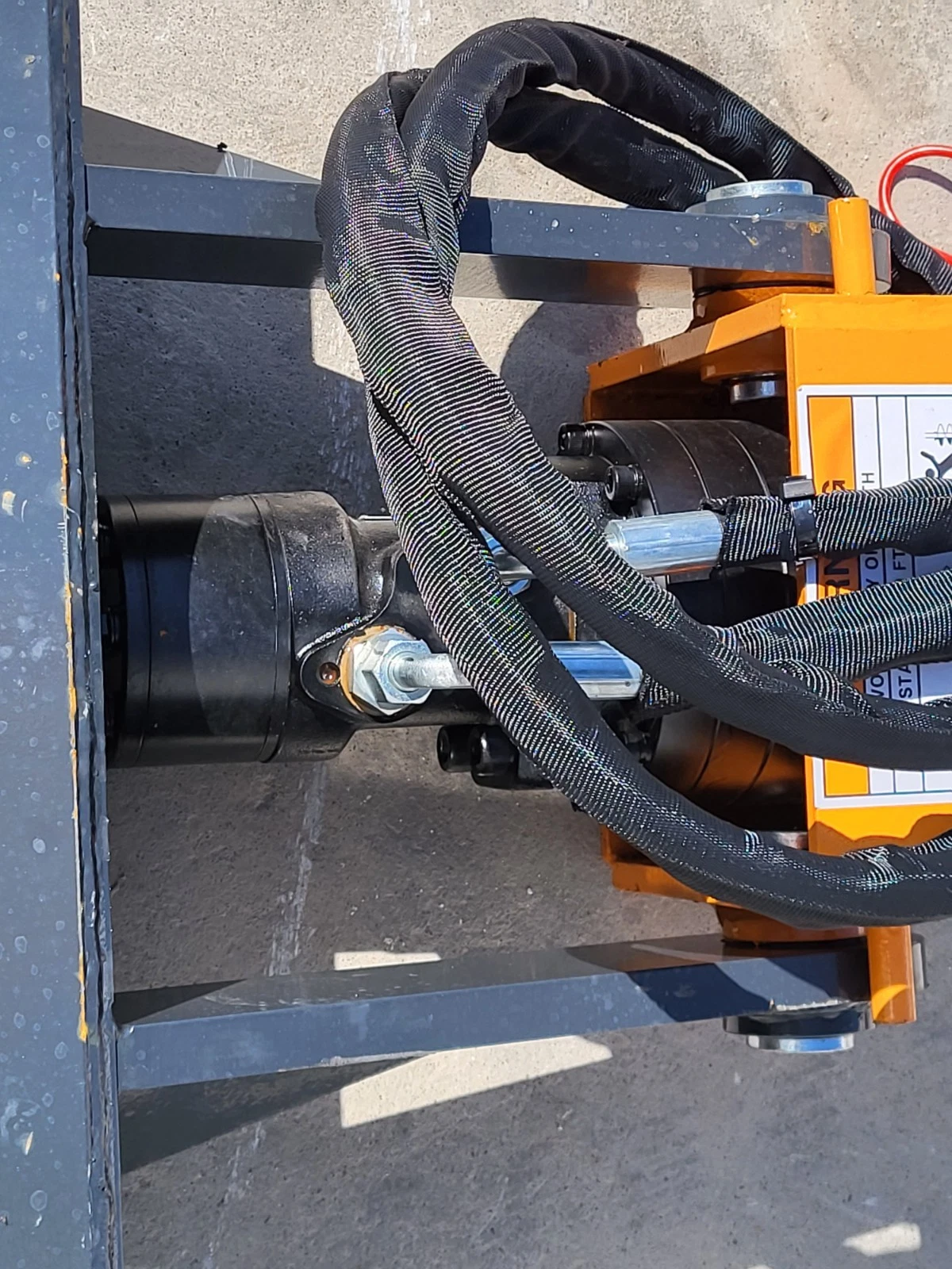 Auger drive's black motor housing bolted to the orange gearbox, sleeved hydraulic hoses looped over the mount frame