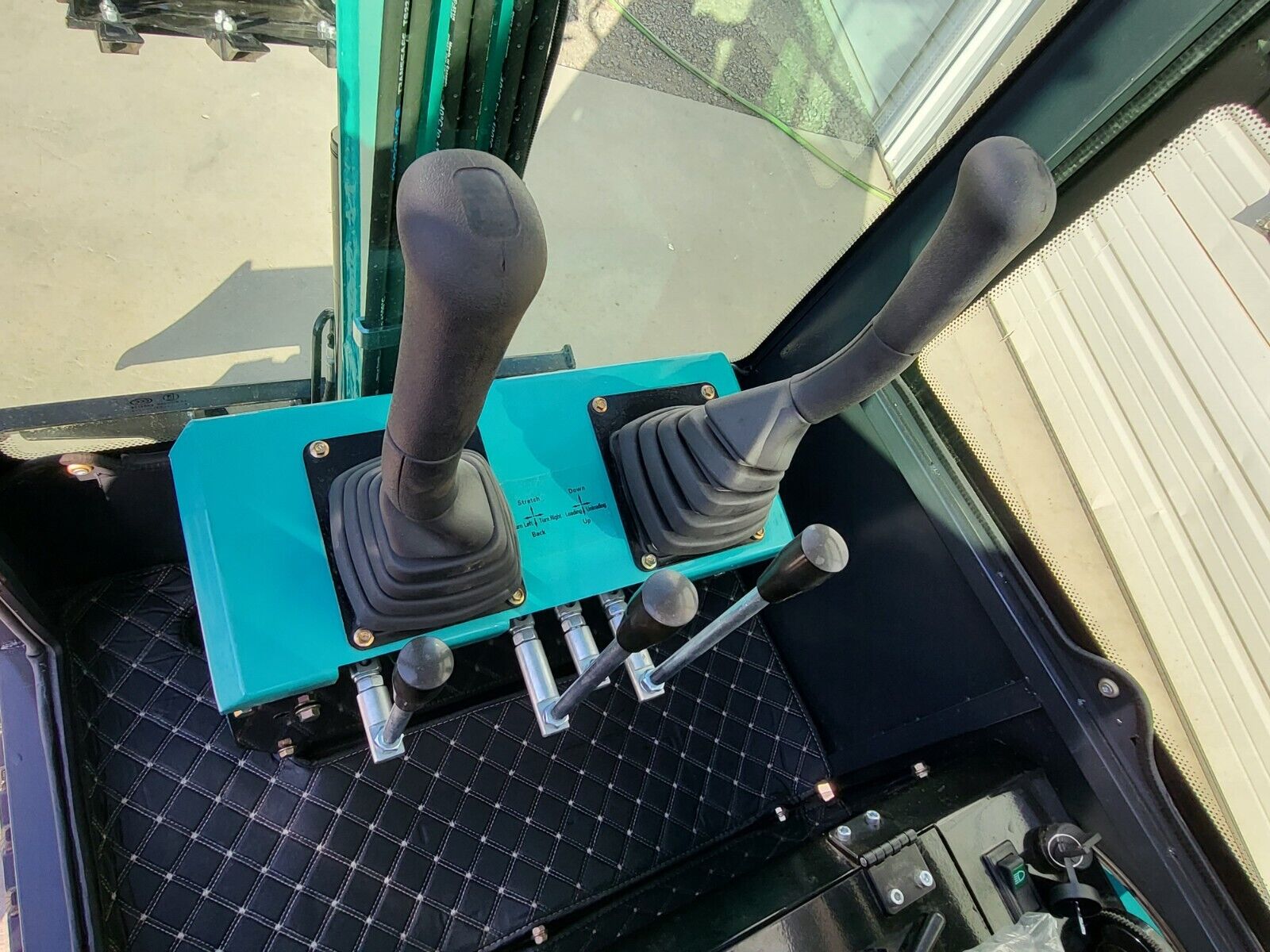 FF13 cab controls: two joysticks on the teal console, travel levers and pedals on the quilted floor mat
