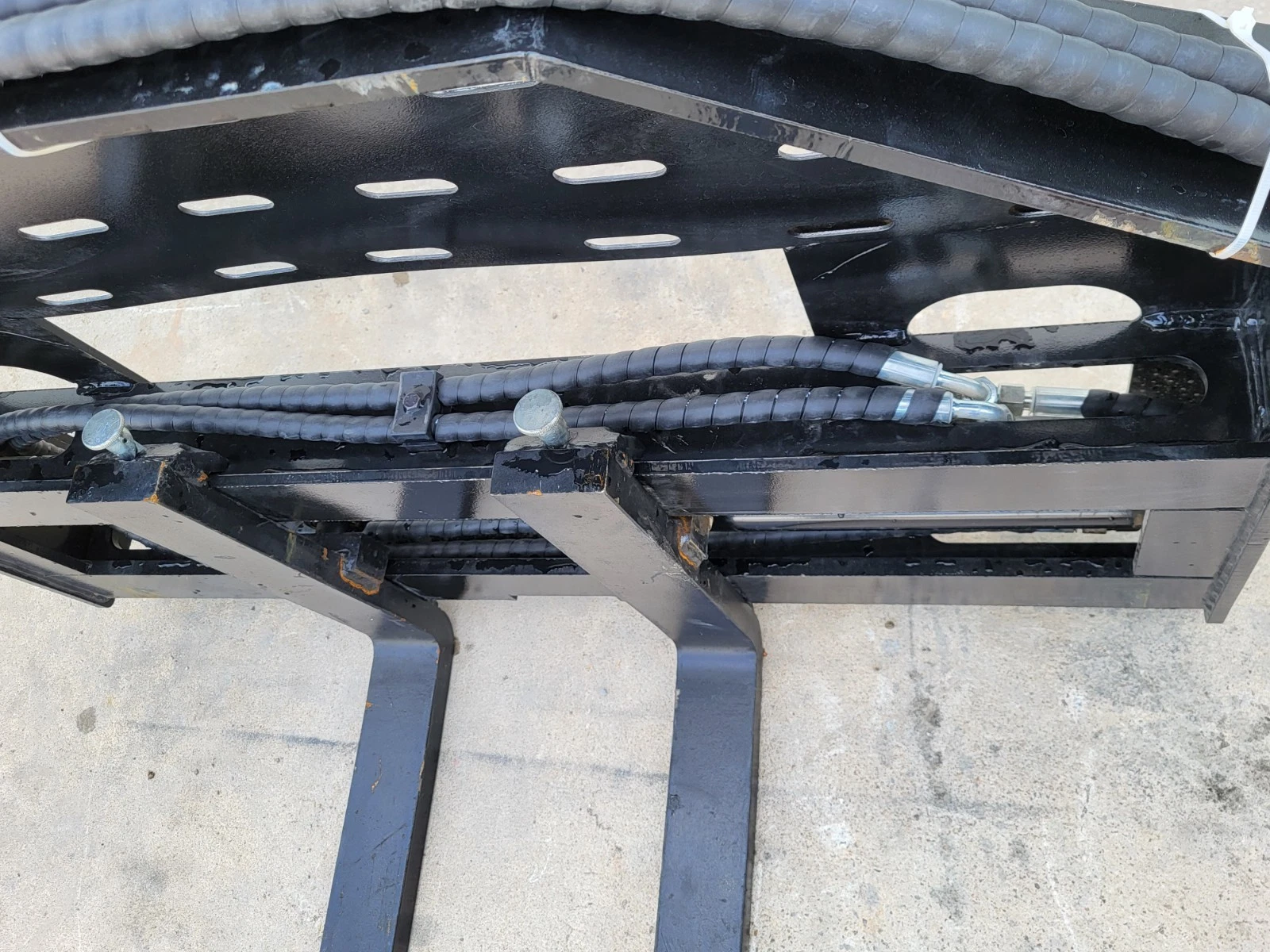 Pallet fork carriage from above: slotted backrest, hose runs, couplers and the two fork hangers