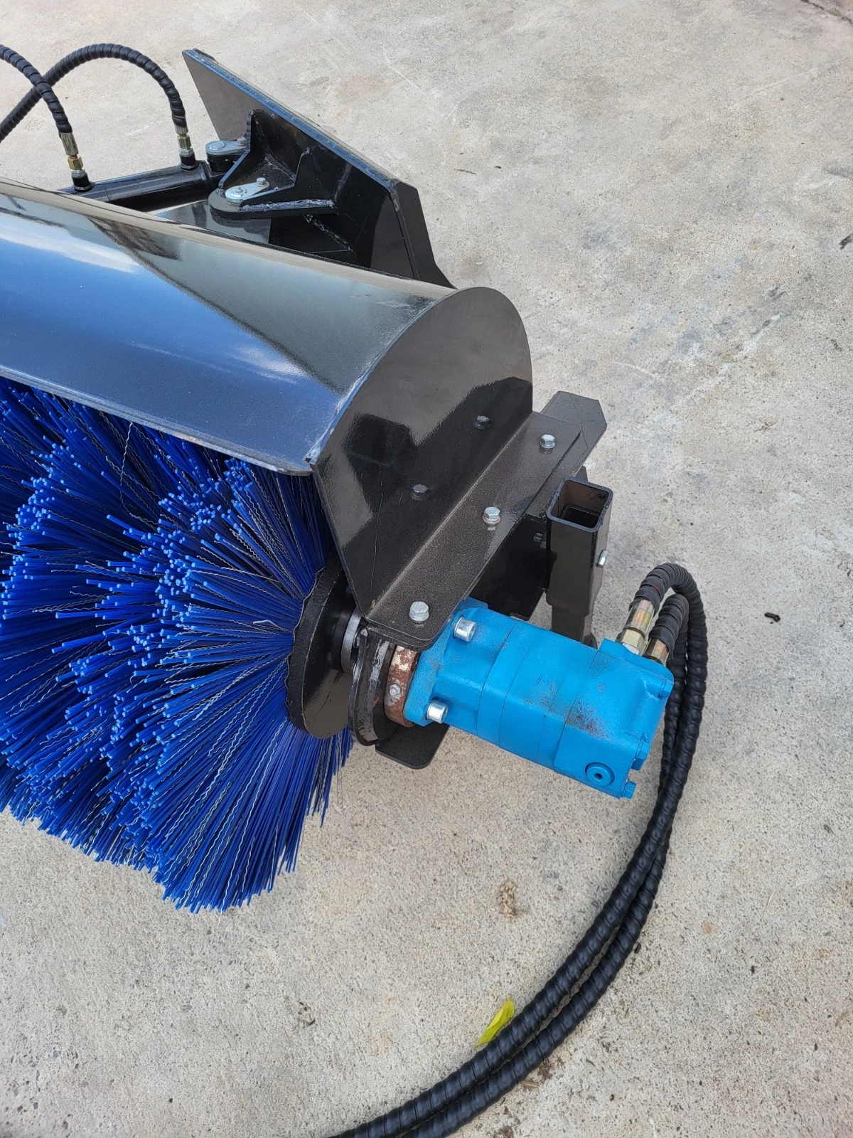 Blue hydraulic drive motor bolted to the angle broom's end plate, driving the blue bristle roller
