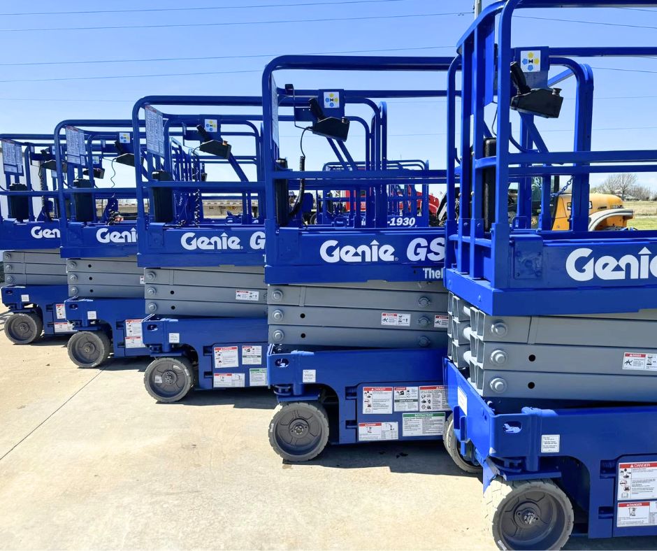 Blue Genie scissor lifts lined up in a row, platforms lowered with guardrails and control boxes on the rails
