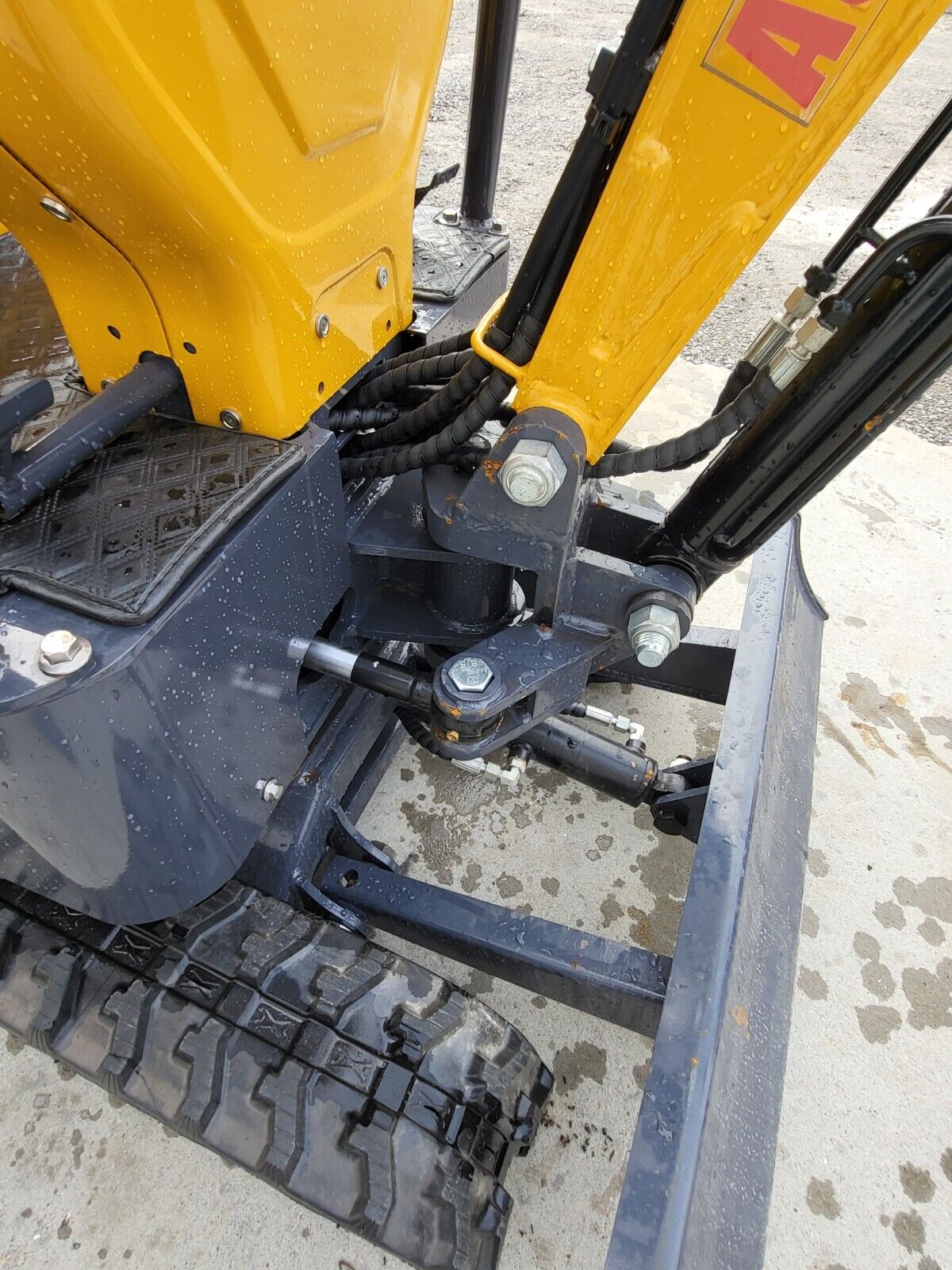 DM12-C boom swing bracket: pivot pin, swing cylinder and routed hydraulic hoses above the rubber track and dozer blade