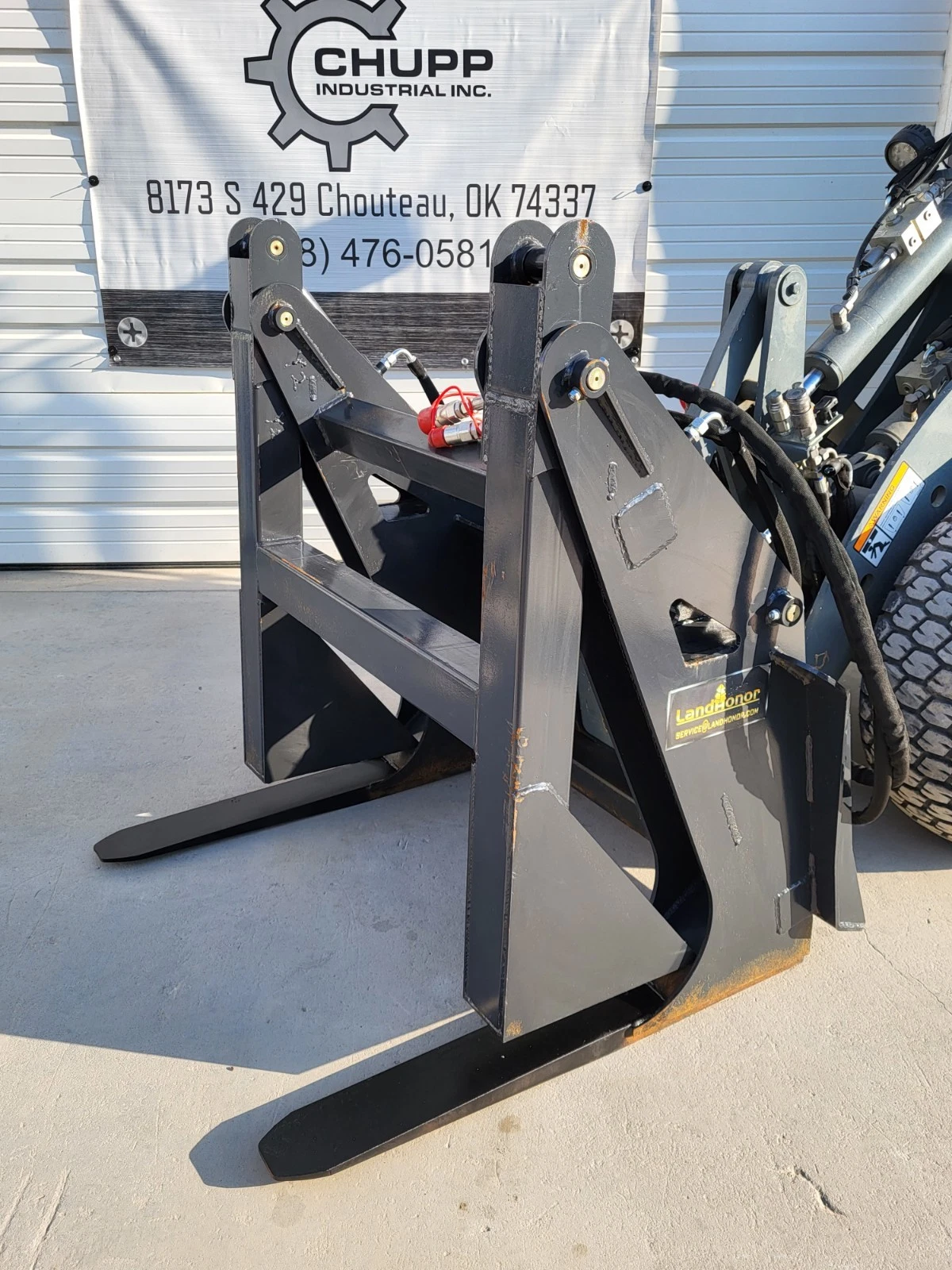 Landhonor log grapple, arms raised over tapered tines with twin cylinders and a red coupler