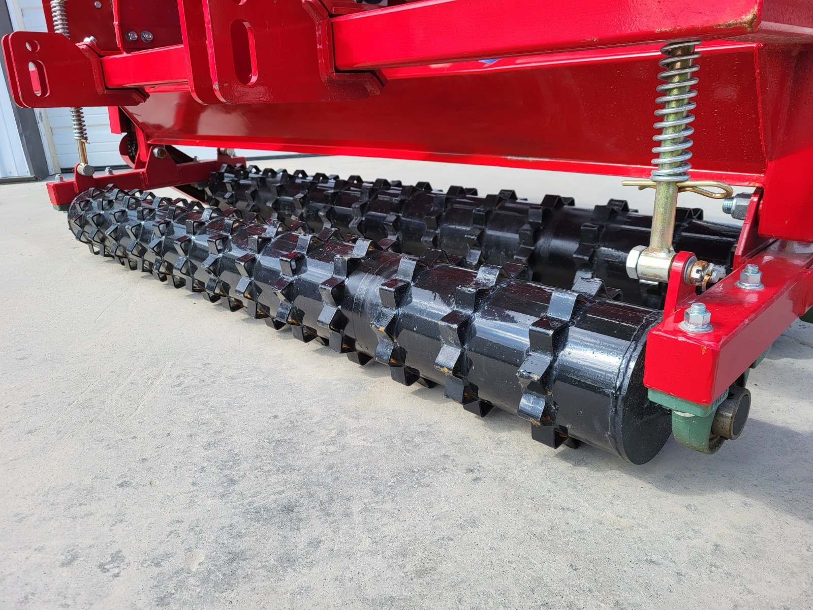No till seed drill toothed packer roller under the red frame with a spring-loaded tension arm