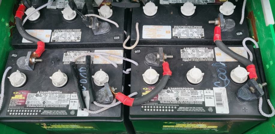 Deep-cycle DC battery bank of the scissor lift, black batteries with red and black cable lugs in a green tray
