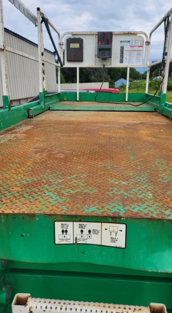 Green steel diamond-plate work platform of the scissor lift, rear control console and load-capacity placards, surface rust