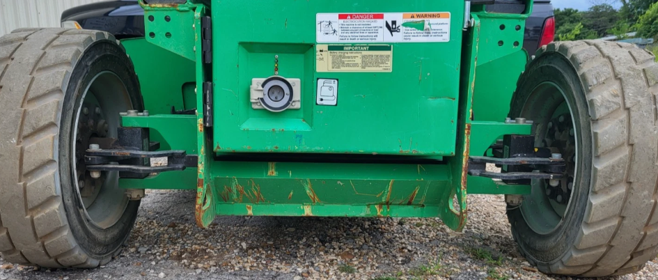 Rear of the green scissor lift, large smooth solid drive tires, rear axle and battery charging port on the green frame