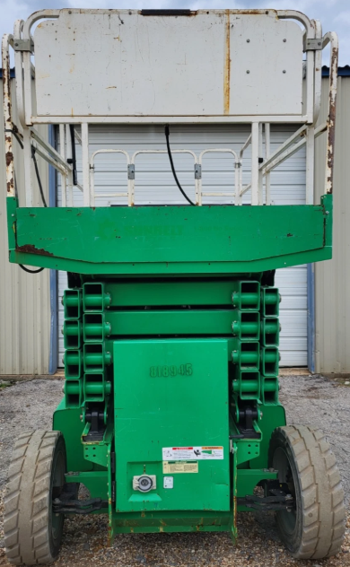 Green JLG scissor lift fully lowered, white folded guardrail platform stacked on the green scissor mechanism, solid tires