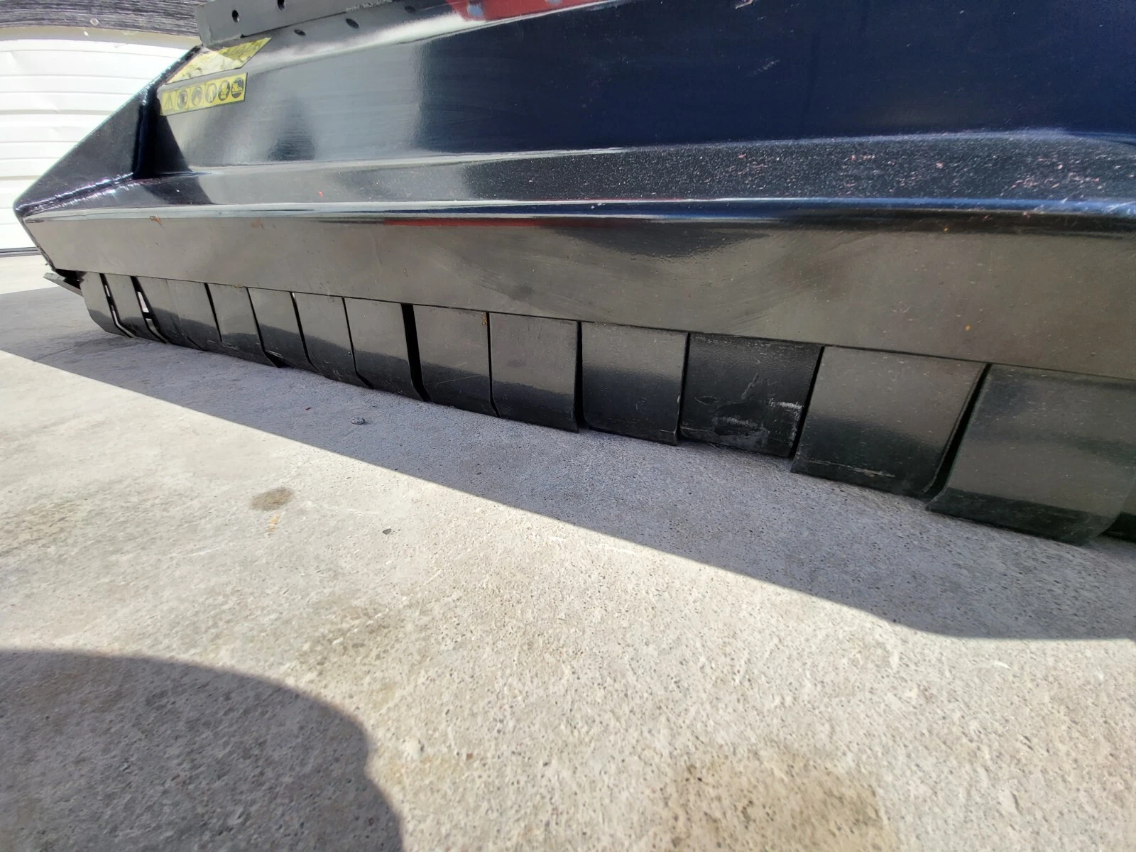 Flail mower deck's lower edge with the row of black rubber guard flaps along the bottom