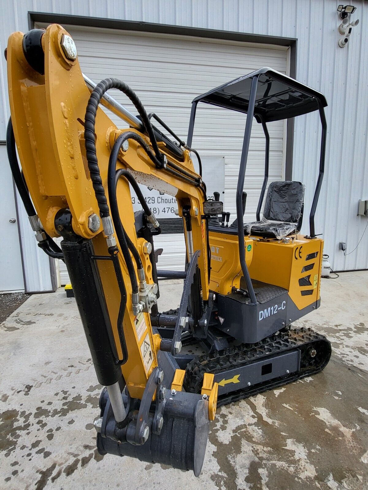 AGT DM12-C mini excavator, boom raised: articulating arm, hydraulic thumb, digging bucket, canopy over the seat, tracks