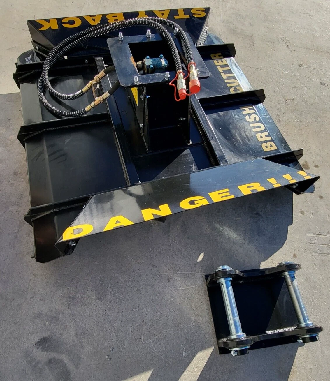 Brush cutter deck at an angle, yellow DANGER and BRUSH CUTTER lettering, twin-pin mounting bracket alongside