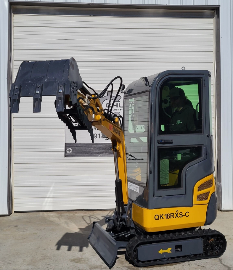 QK18RXS-C mini excavator with an operator in the cab, boom raised and the hydraulic thumb clamped over the bucket