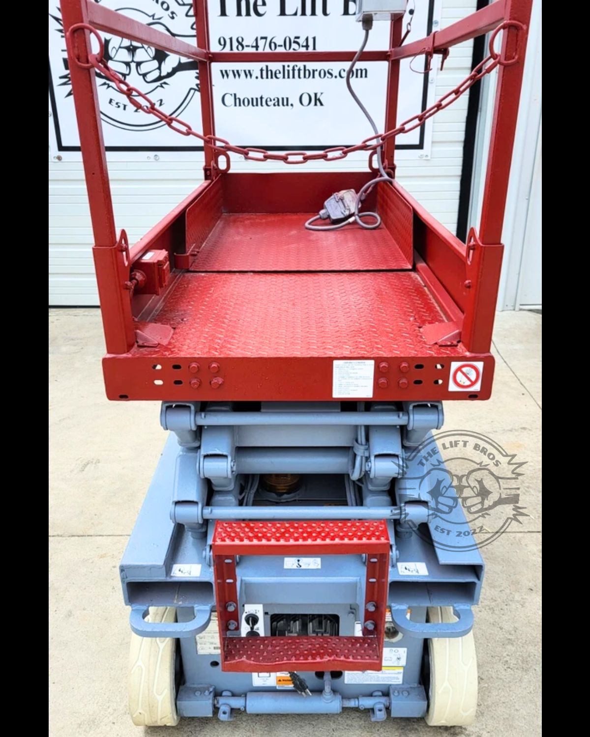 Skyjack scissor lift red diamond-plate platform deck with chain entry gate and ground control panel below
