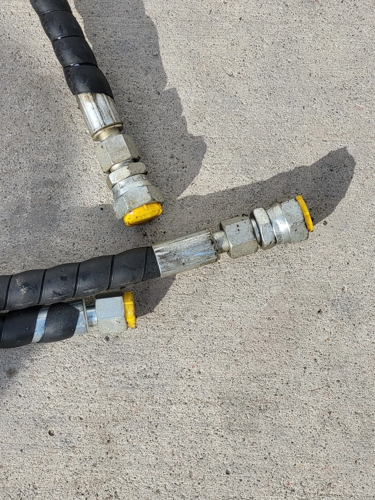 Two hydraulic supply hoses in black spiral wrap, steel couplers capped with yellow dust plugs