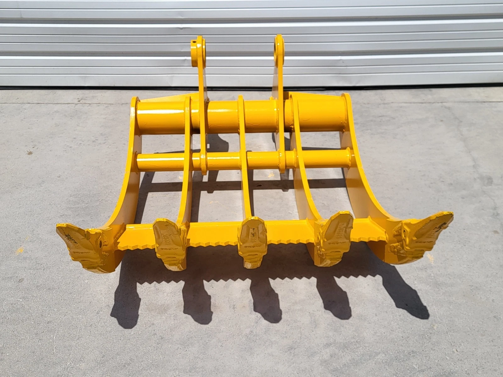Yellow rake from behind: cross tubes, twin mounting lugs and five tine tips over a serrated edge