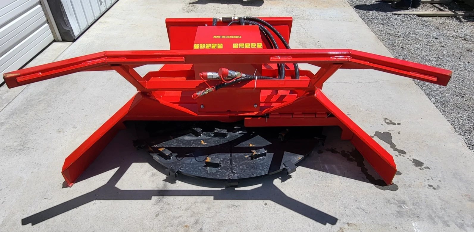 Red disc mulcher from the rear: push frame arms, hydraulic couplers and the toothed cutting disc beneath