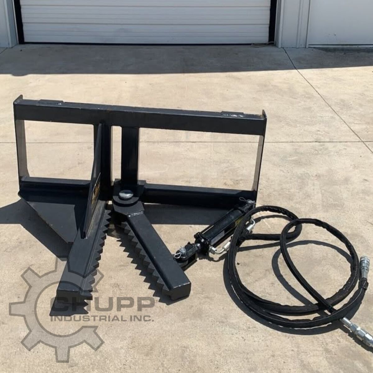 Tree and post puller: two serrated steel jaws open on the frame, hydraulic cylinder and coiled hoses alongside