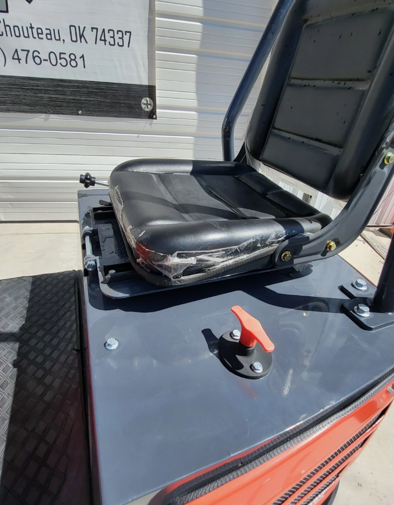 MX15R mini excavator operator seat, still factory-wrapped, on the gray deck beside a red control lever