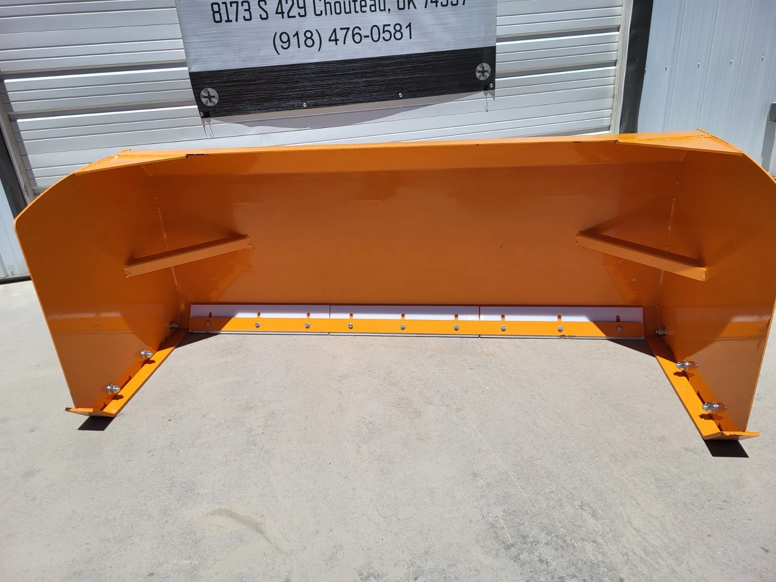 Snow plow blade straight on: orange moldboard, ribbed supports and a white poly cutting edge