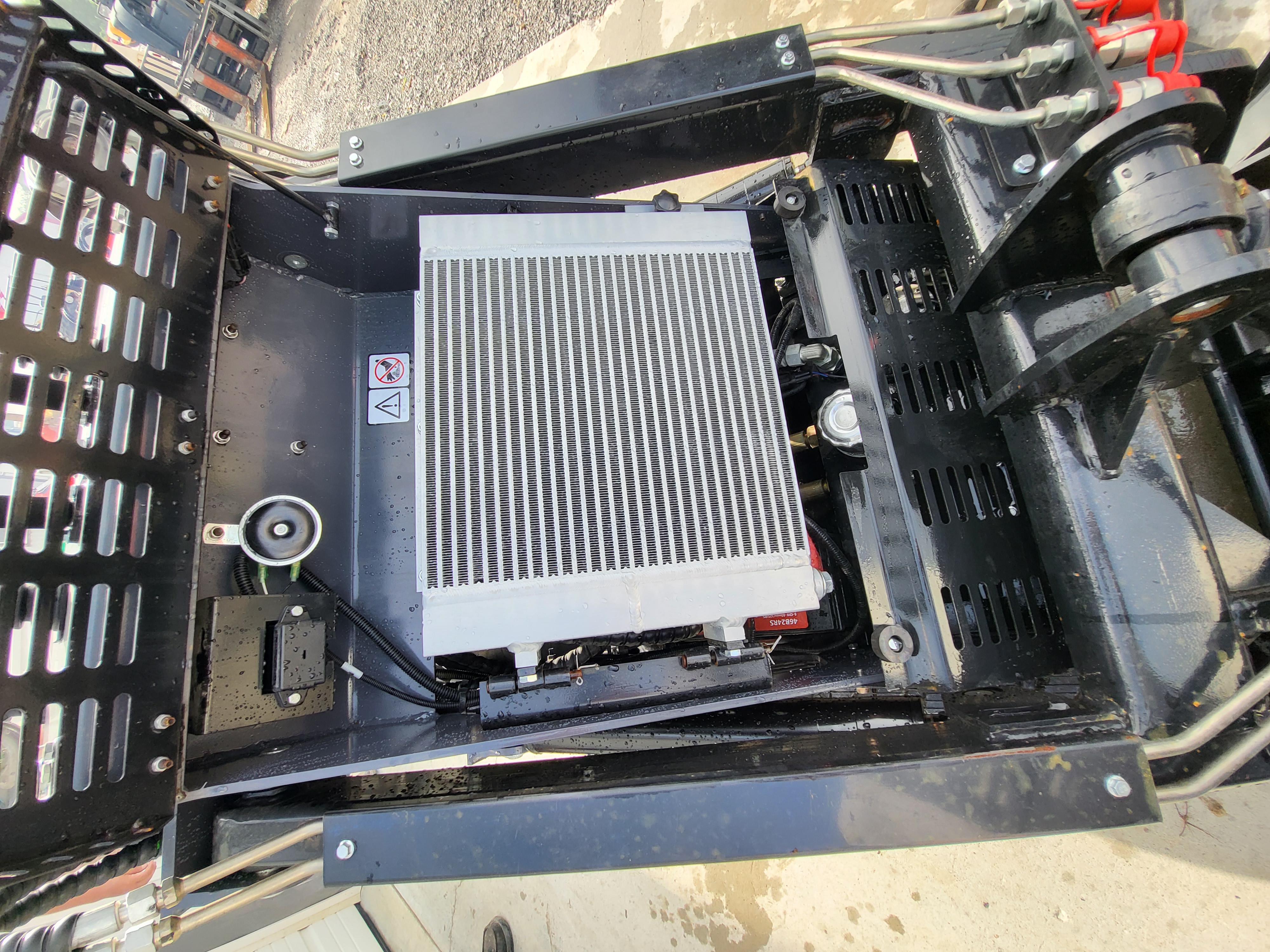 KRT23 mini skid steer engine bay: aluminum hydraulic oil cooler, battery and hydraulic lines under the open cover