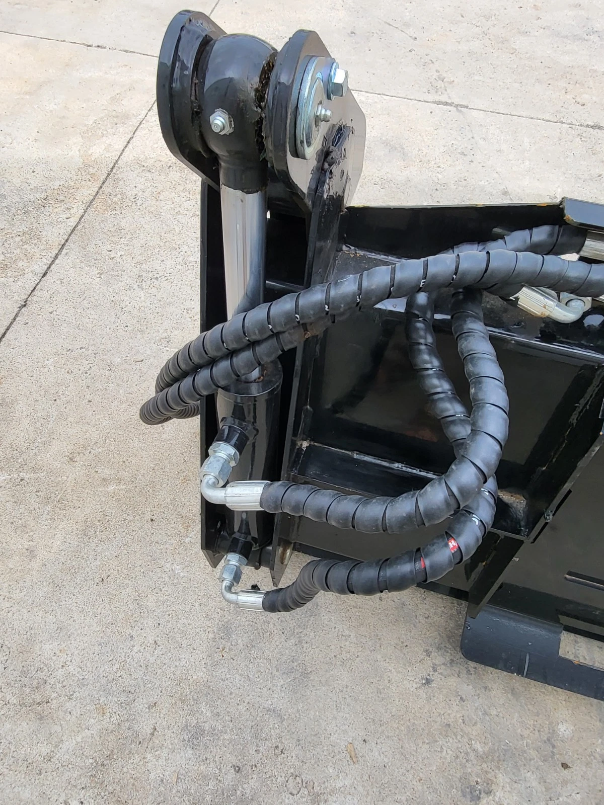 Clamshell cylinder and pivot at the 4-in-1 bucket's corner, sleeved hose runs looped over the frame