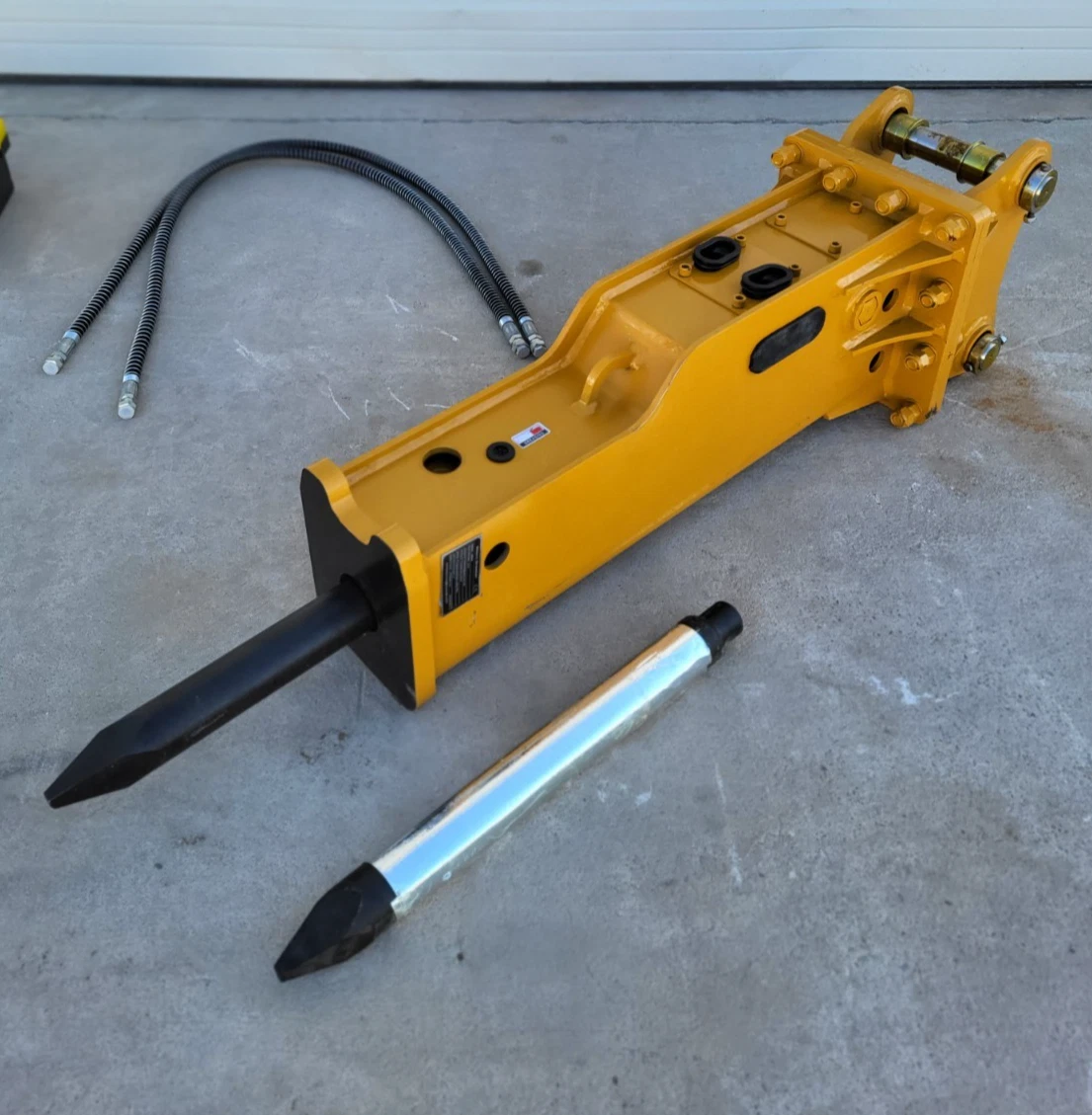 Yellow SB45 hydraulic breaker with mounting bracket and pins, moil chisel fitted, spare chisel and coiled hoses