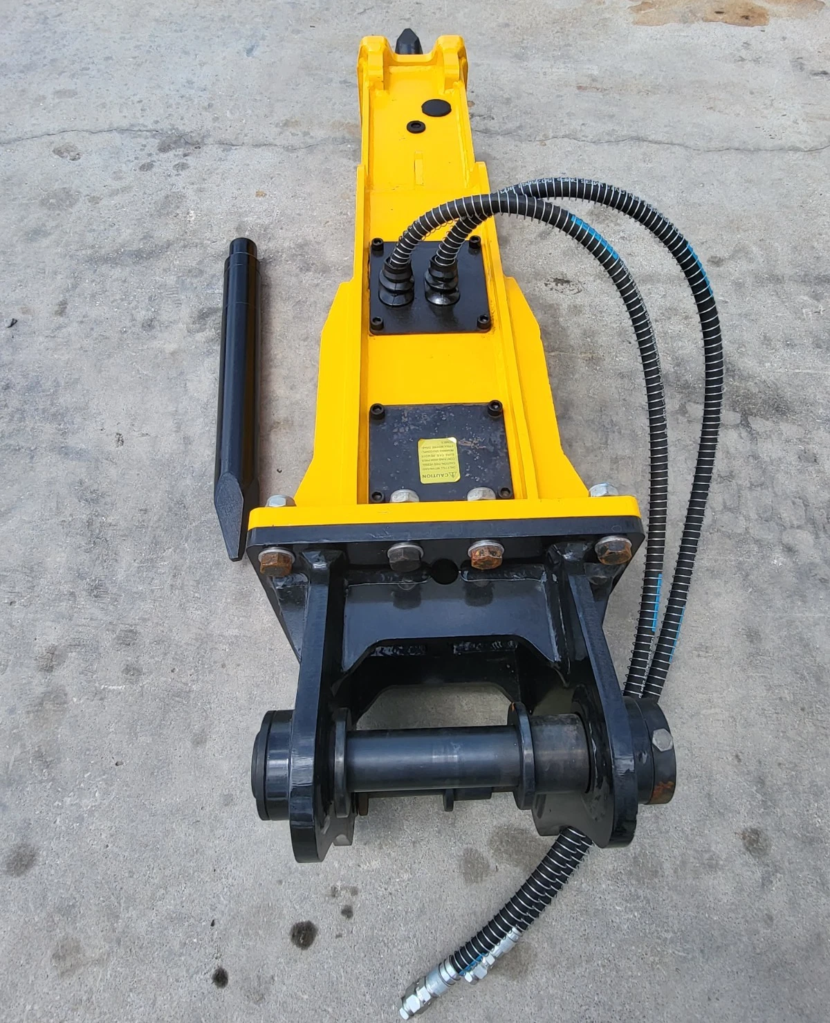 TOFT750 breaker from above: bolted valve plates, caution decal, black mounting bracket with pin and hoses