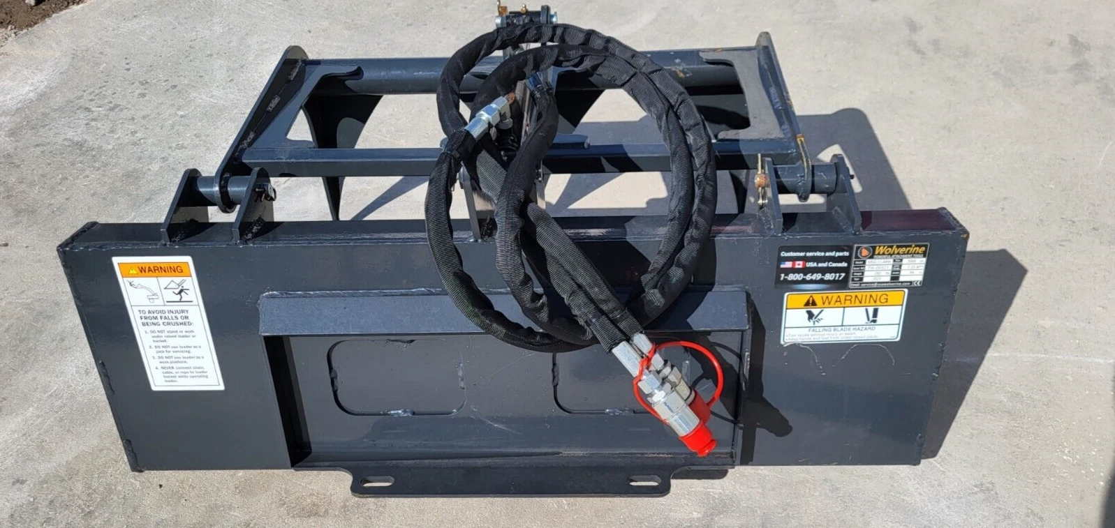 Back of the gray attachment: mount plate, coiled hydraulic hoses, red coupler and warning decals