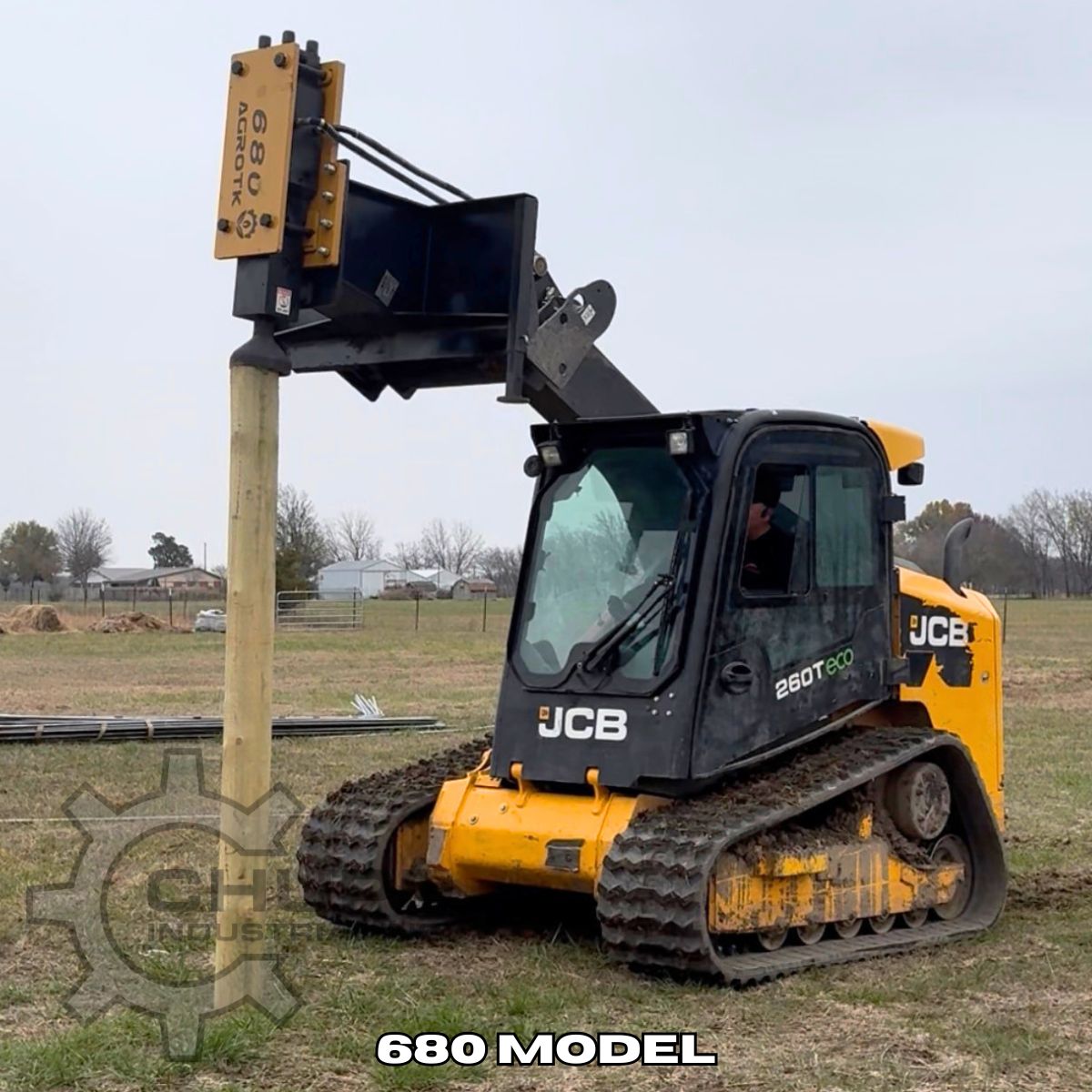 AGROTK 680 post driver mounted on a JCB compact track loader, driving a wooden fence post into the ground