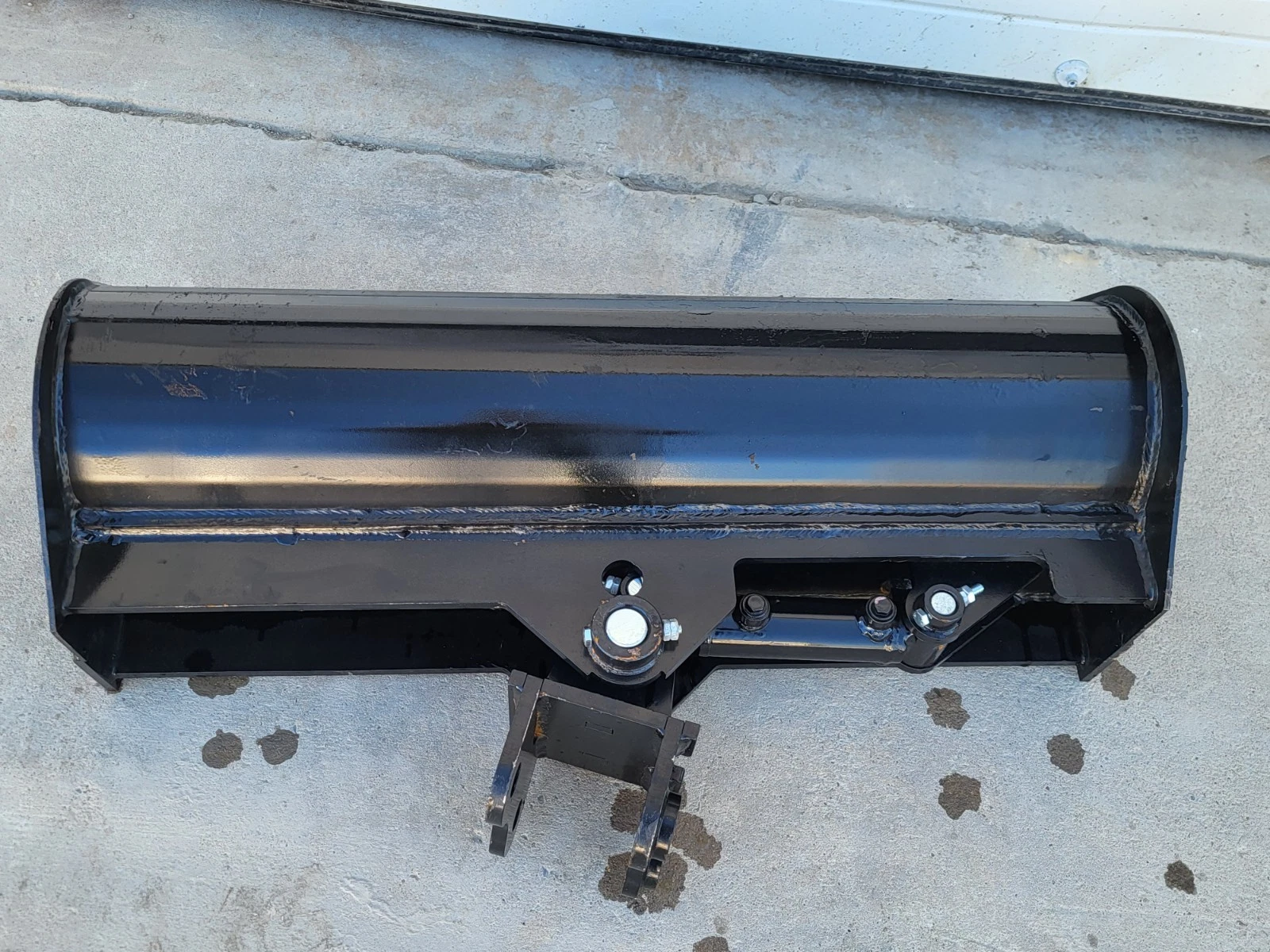 Back of the 32-inch tilt bucket: welded steel shell, center pivot, tilt cylinder and twin-pin bracket below