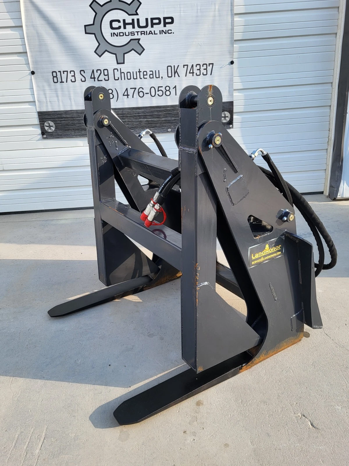 Log grapple with clamp arms raised above the tapered tines, twin cylinders on the quick-attach plate