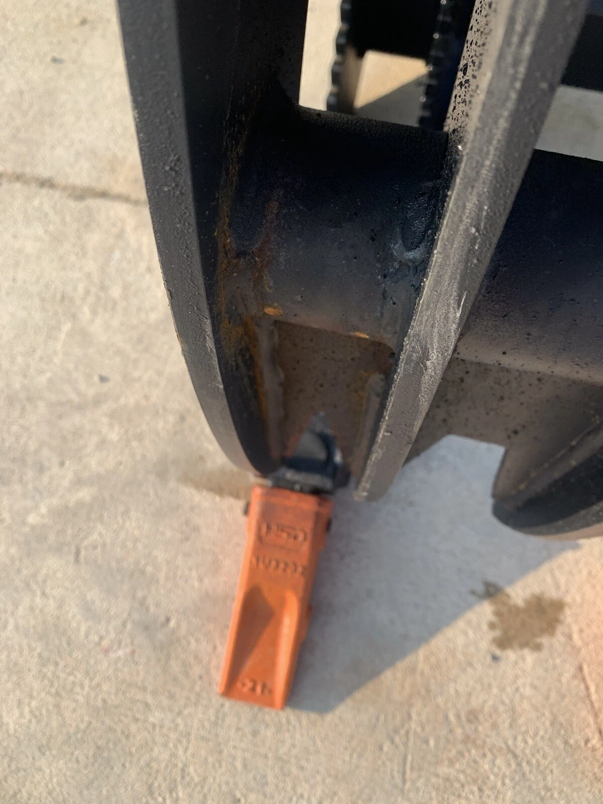 Grapple bucket tine end with an orange bolt-on tooth, serrated grapple arm above