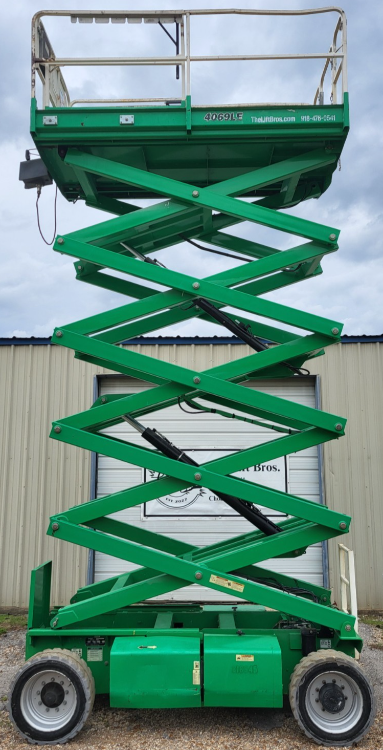 Green JLG 4069LE rough terrain scissor lift fully extended, platform raised high on green scissor stack