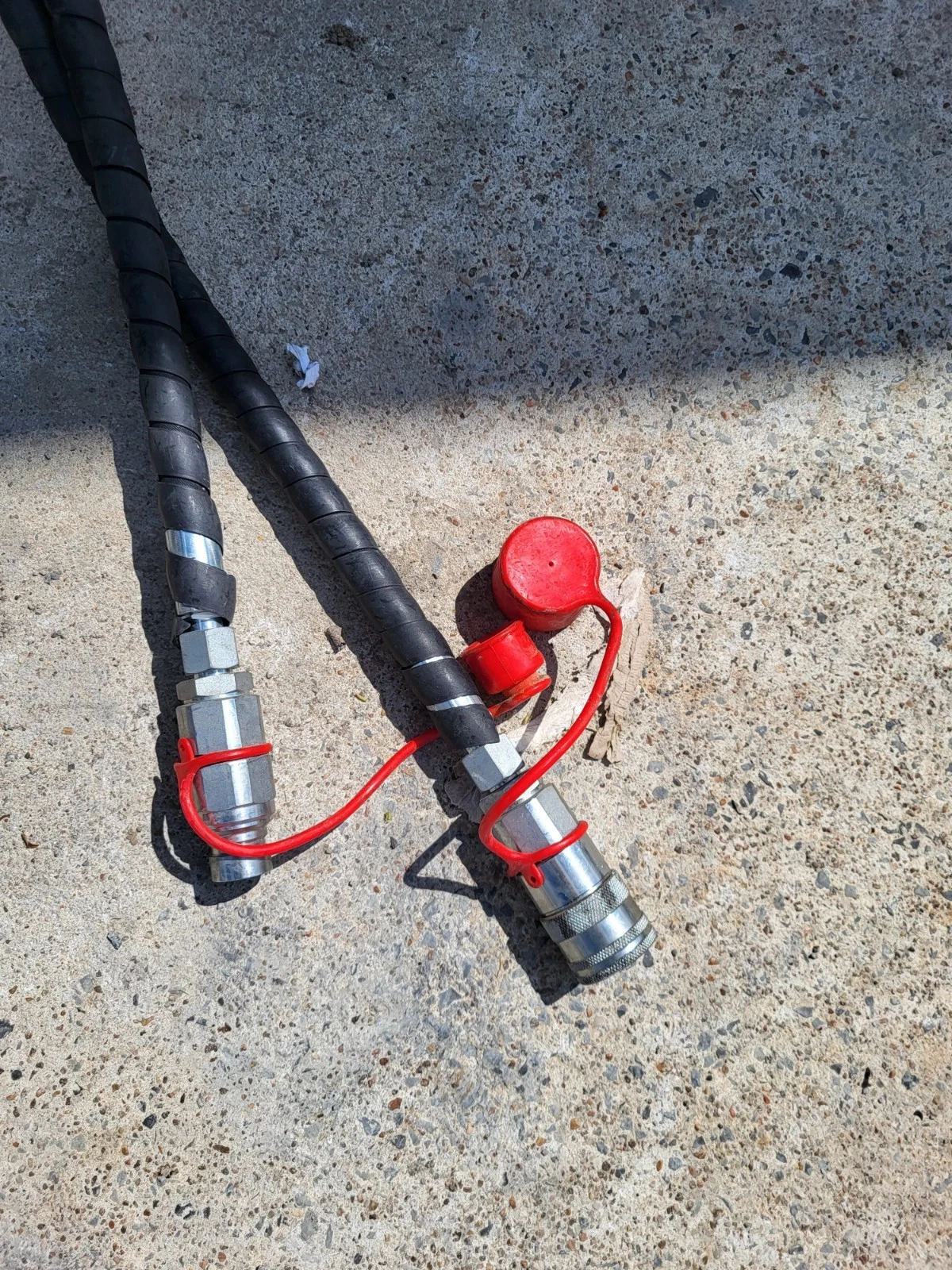 Two hydraulic hoses with red-capped quick couplers, one cap unplugged