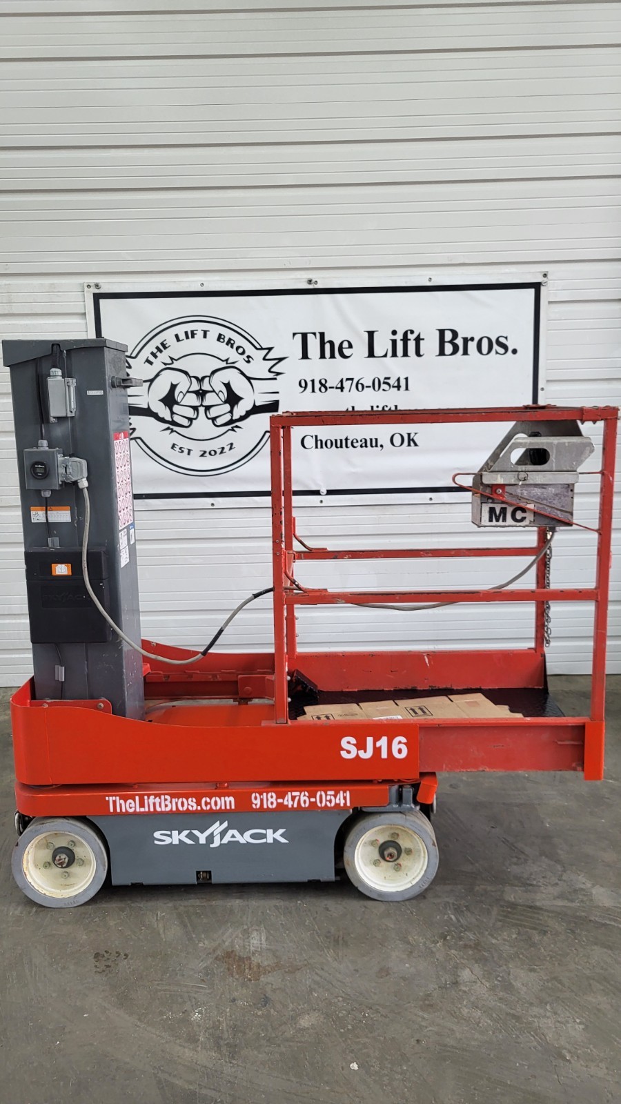 Orange Skyjack SJ16 vertical mast lift, side view, mast stowed, platform with material carrier