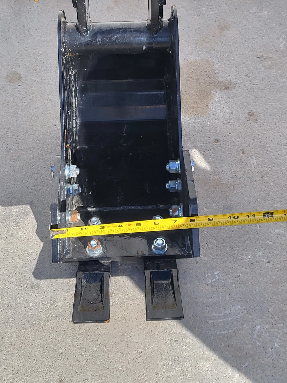 Tape measure across the base of the 8-inch trenching bucket, running past the eleven-inch mark