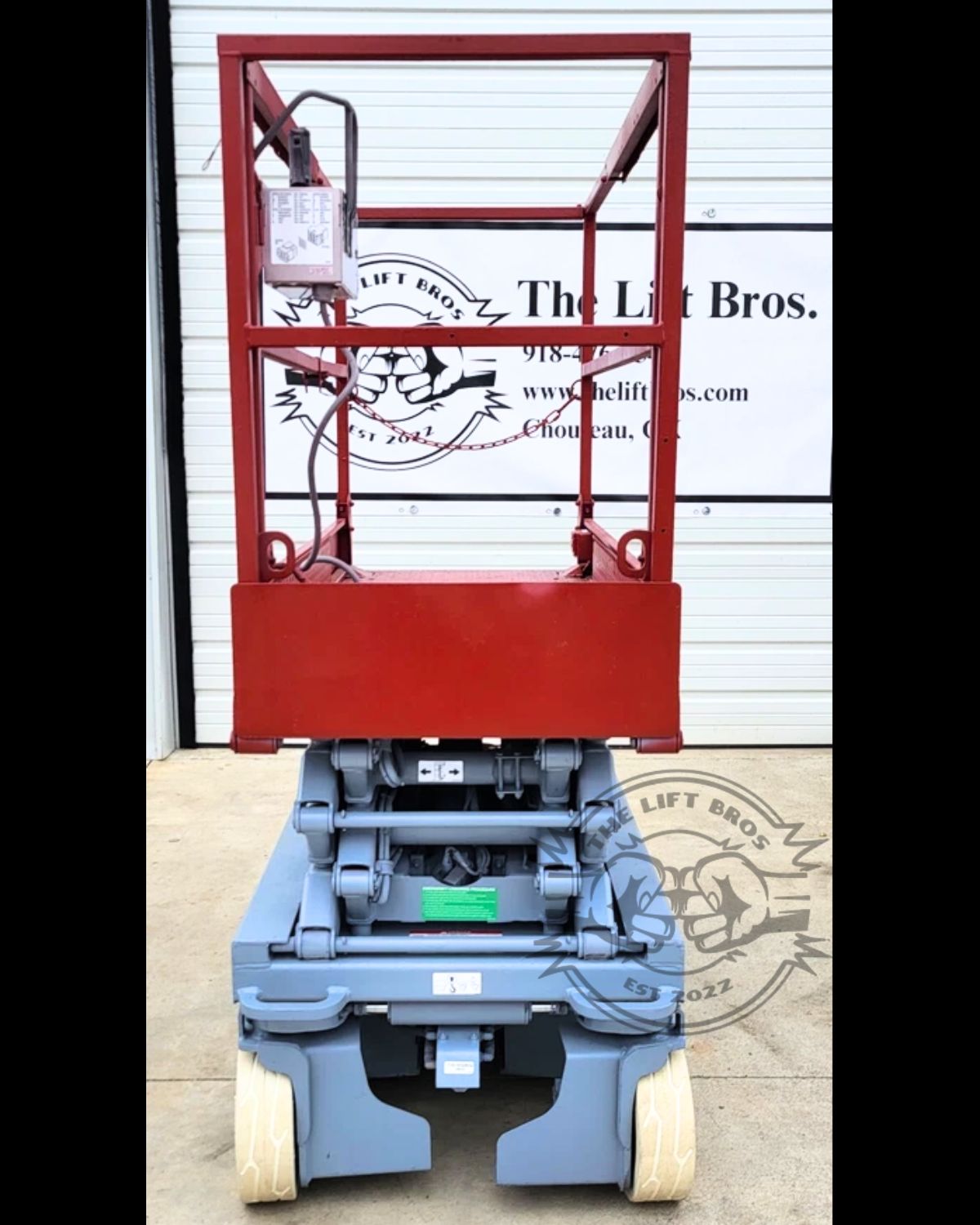 Skyjack scissor lift lowered: red platform with guardrails, upper control box and chain entry gate
