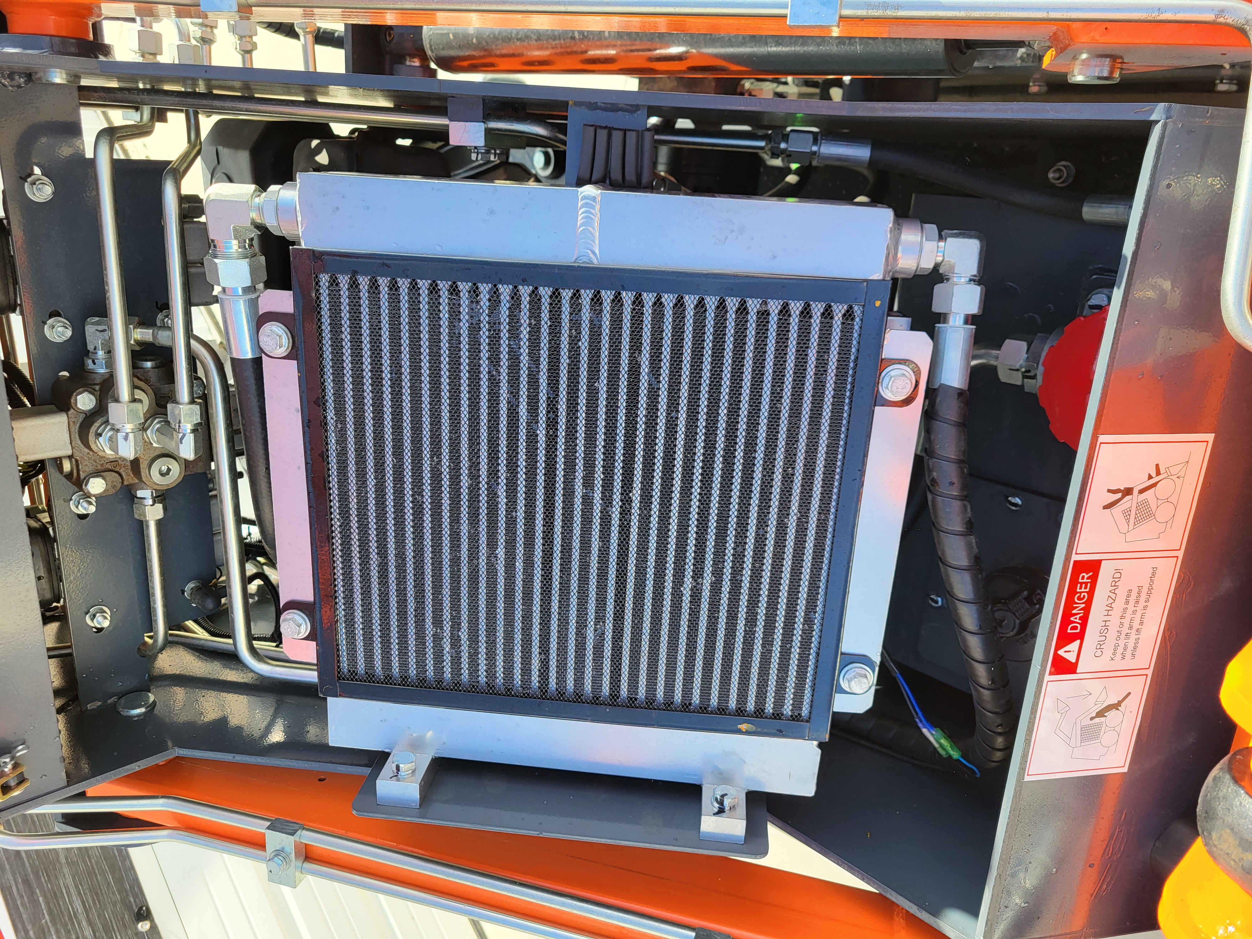AGT YSRT14 hydraulic oil cooler mounted in the engine bay with steel lines and a crush-hazard warning decal