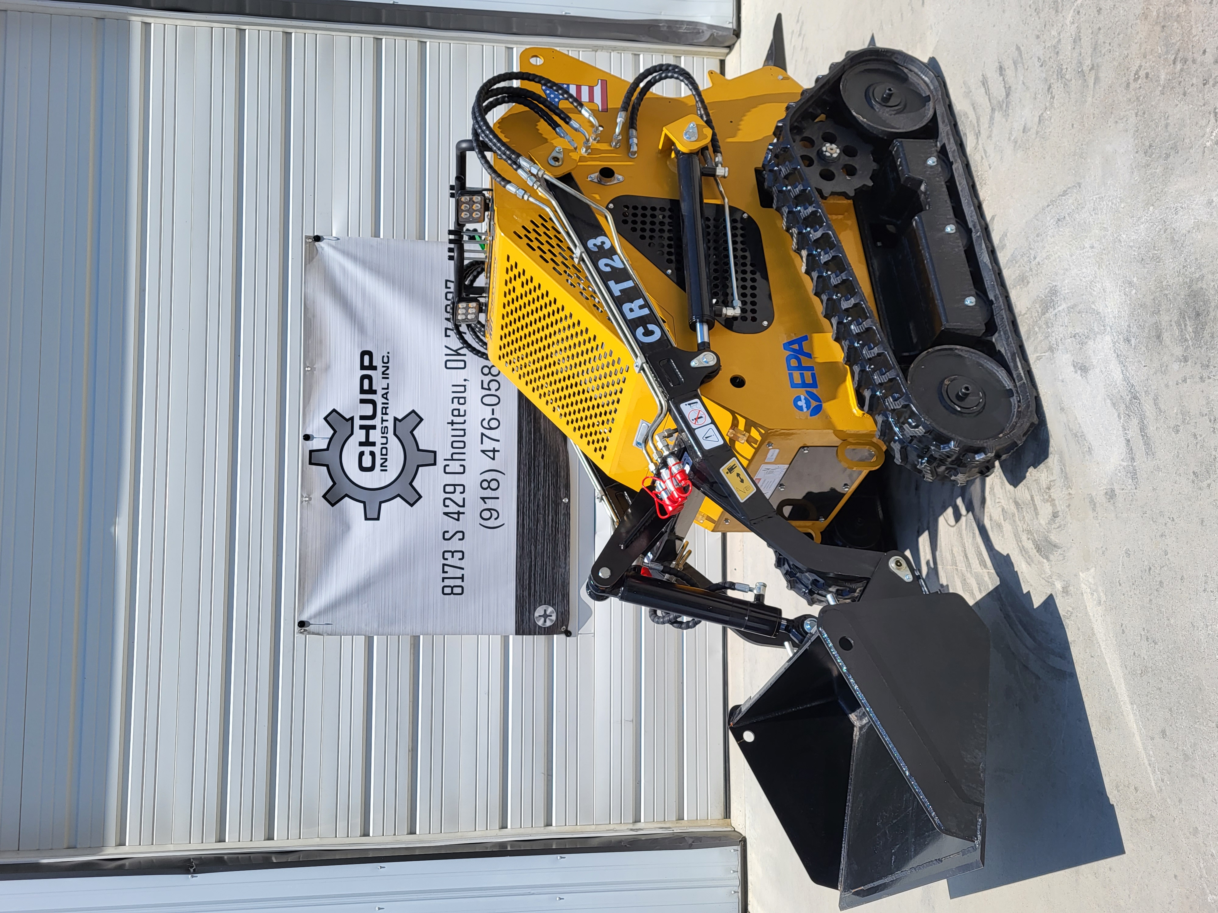 AGT CRT23 mini skid steer from the side: loader arms down with the dirt bucket flat, perforated hood and rubber tracks