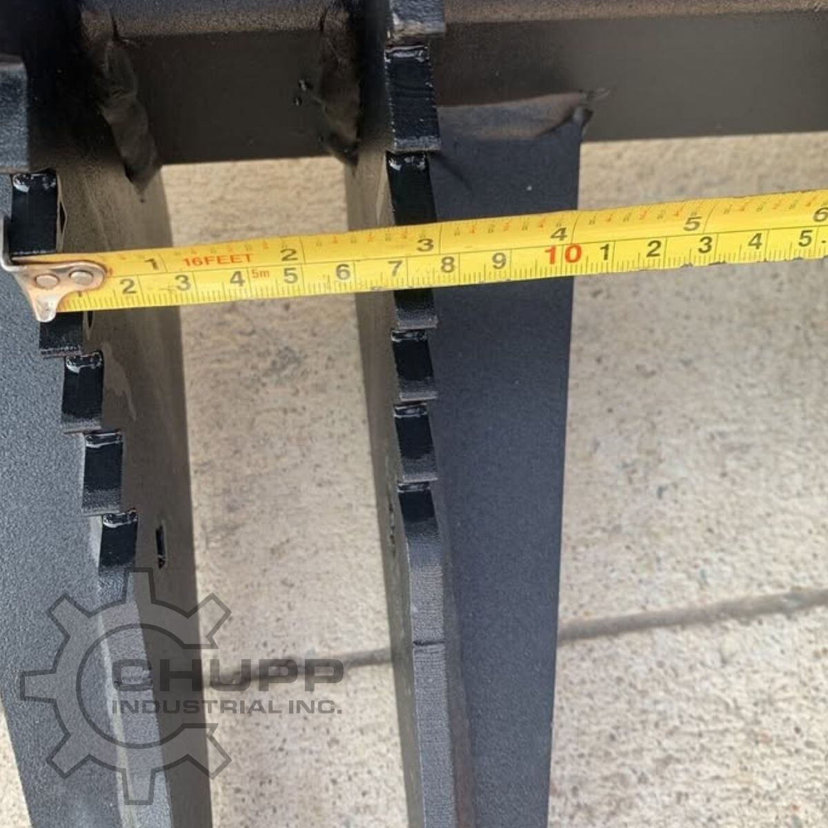 Greatbear grapple rake tine spacing measured with a tape; welded wear tabs run along the tine edges